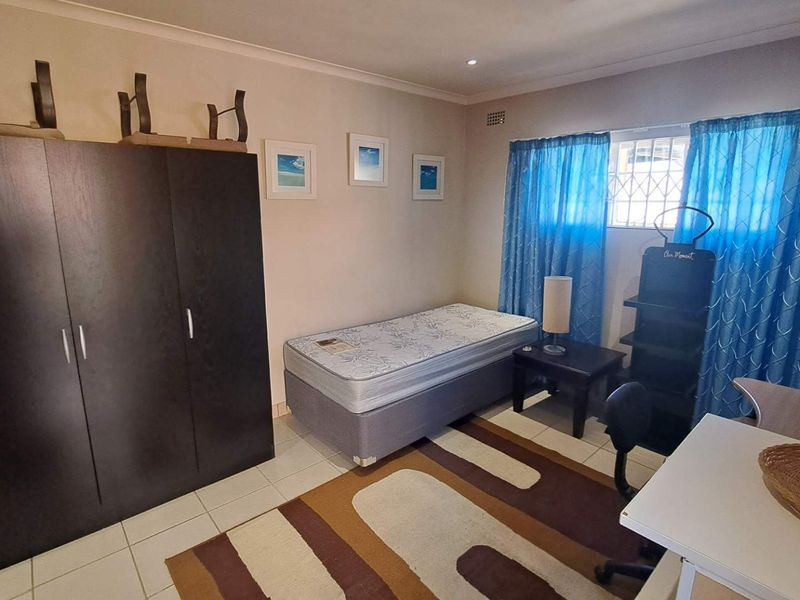A functional bedroom featuring tiled flooring, a built-in wardrobe, and a window fitted with a security gate.