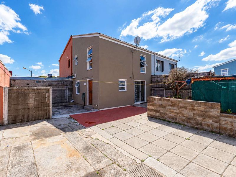 Rear exterior view of the property featuring a paved patio area, boundary walls, and a multi-story building facade with casement windows.