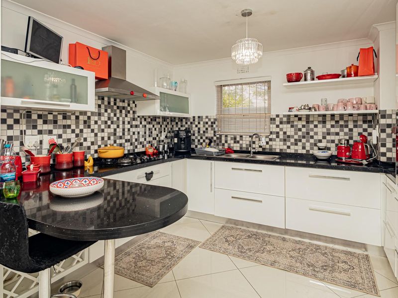 Modern kitchen featuring white gloss cabinetry, black granite countertops, a striking checkerboard mosaic backsplash, and integrated stainless steel appliances.