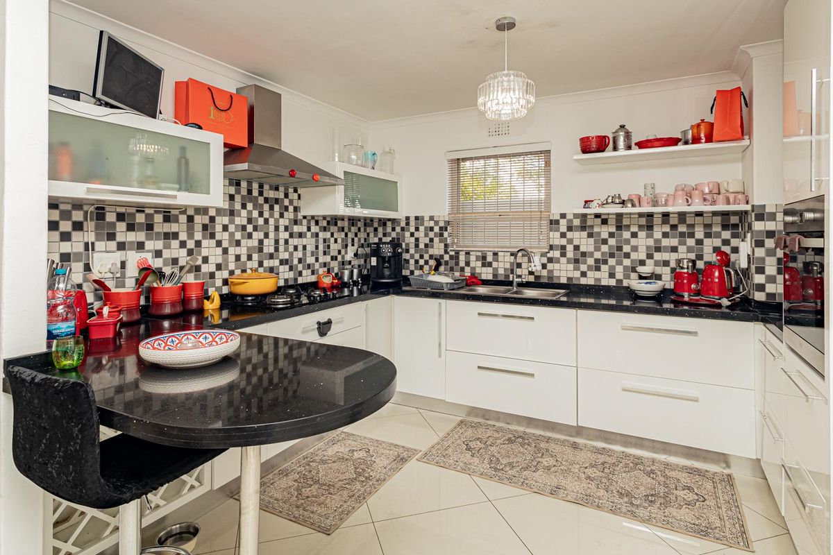 Modern kitchen featuring white gloss cabinetry, black granite countertops, a striking checkerboard mosaic backsplash, and integrated stainless steel appliances.