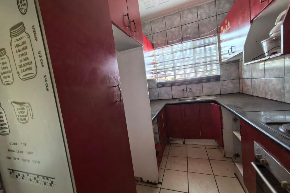 A dated kitchen featuring red cabinetry, tiled backsplash, and built-in oven, requiring cosmetic updates to modernize the space.