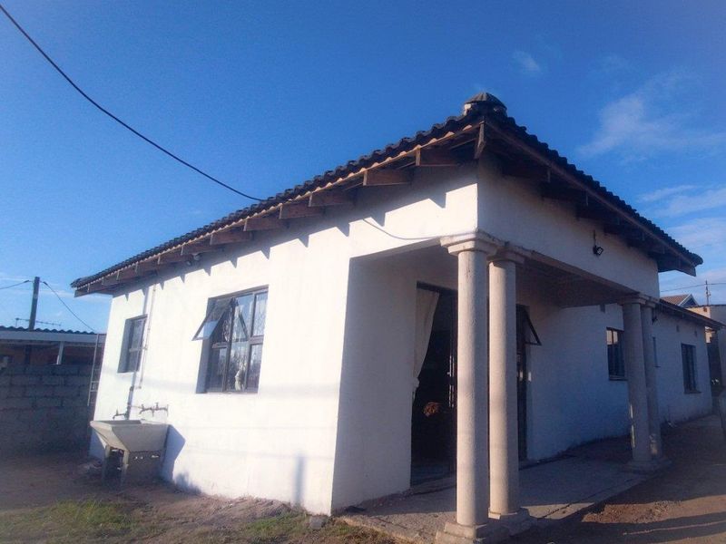 Front view of a single-story house featuring a covered porch with concrete columns, tiled roof, and an external utility sink.