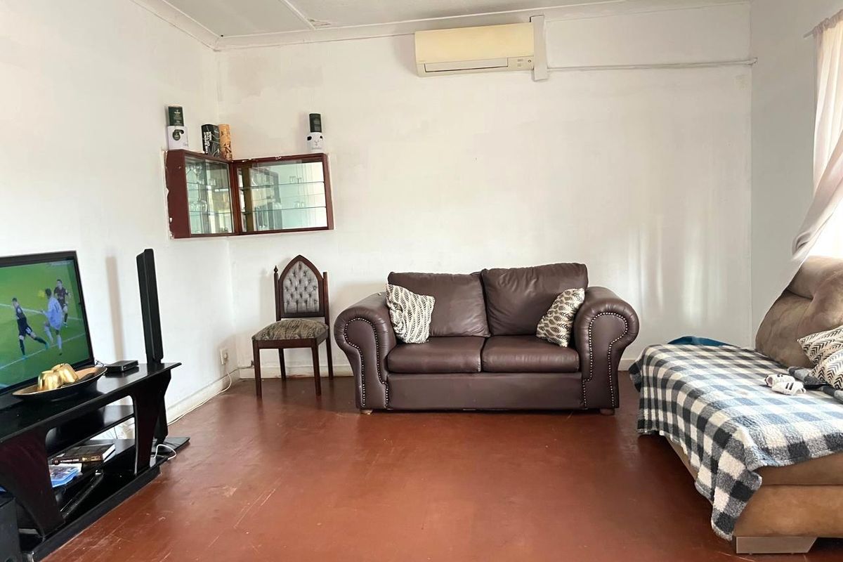 A living room featuring a wall-mounted air conditioning unit, built-in wall cabinetry, and coved ceilings, with worn flooring throughout.