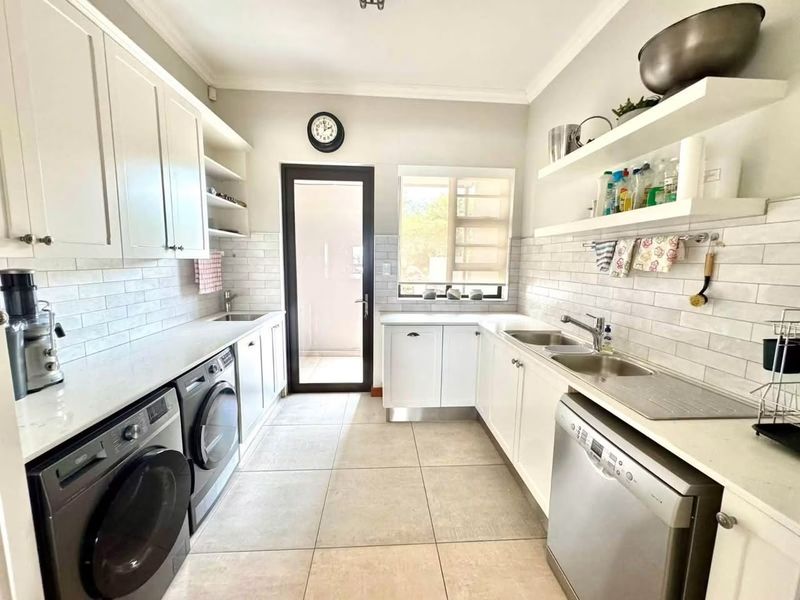 A well-appointed laundry room featuring white cabinetry, stone countertops, subway tile backsplash, and a double stainless steel sink with direct outdoor access.