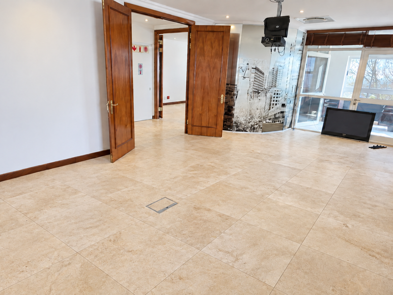 Spacious office area featuring neutral tiled flooring, recessed lighting, and double wooden doors leading to an adjacent room with large windows and natural light.