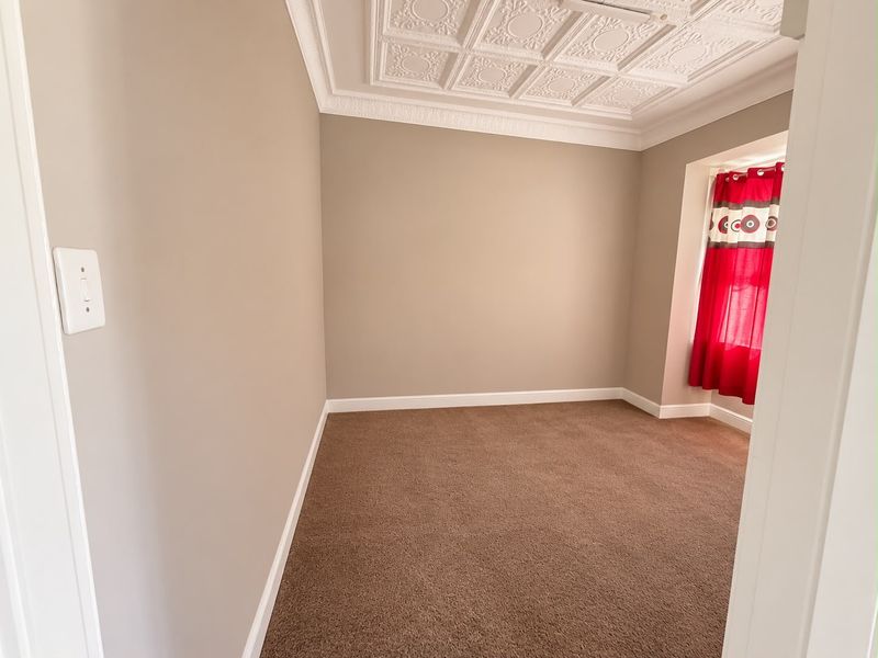 A clean, empty bedroom featuring decorative ceiling tiles, crown molding, and neutral wall tones, providing a versatile space ready for personalization.