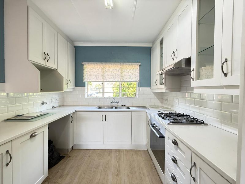 A clean, well-lit kitchen featuring white shaker-style cabinetry, subway tile backsplash, integrated gas hob, and oven, with wood-look laminate flooring.