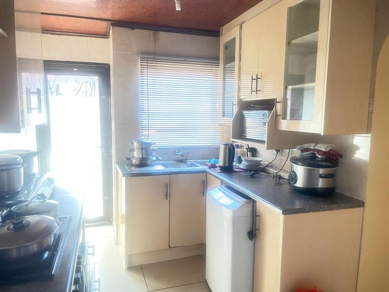 A compact kitchen featuring built-in cabinetry, laminate countertops, and tiled finishes. The space requires cosmetic updates to modernize the dated fixtures and surfaces.