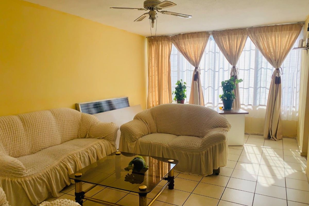 A living room featuring large windows with natural light, tiled flooring, and a ceiling fan.