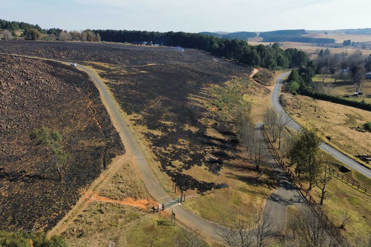 Aerial view of a large rural property featuring paved access roads, perimeter fencing, and significant areas of land affected by recent fire damage.