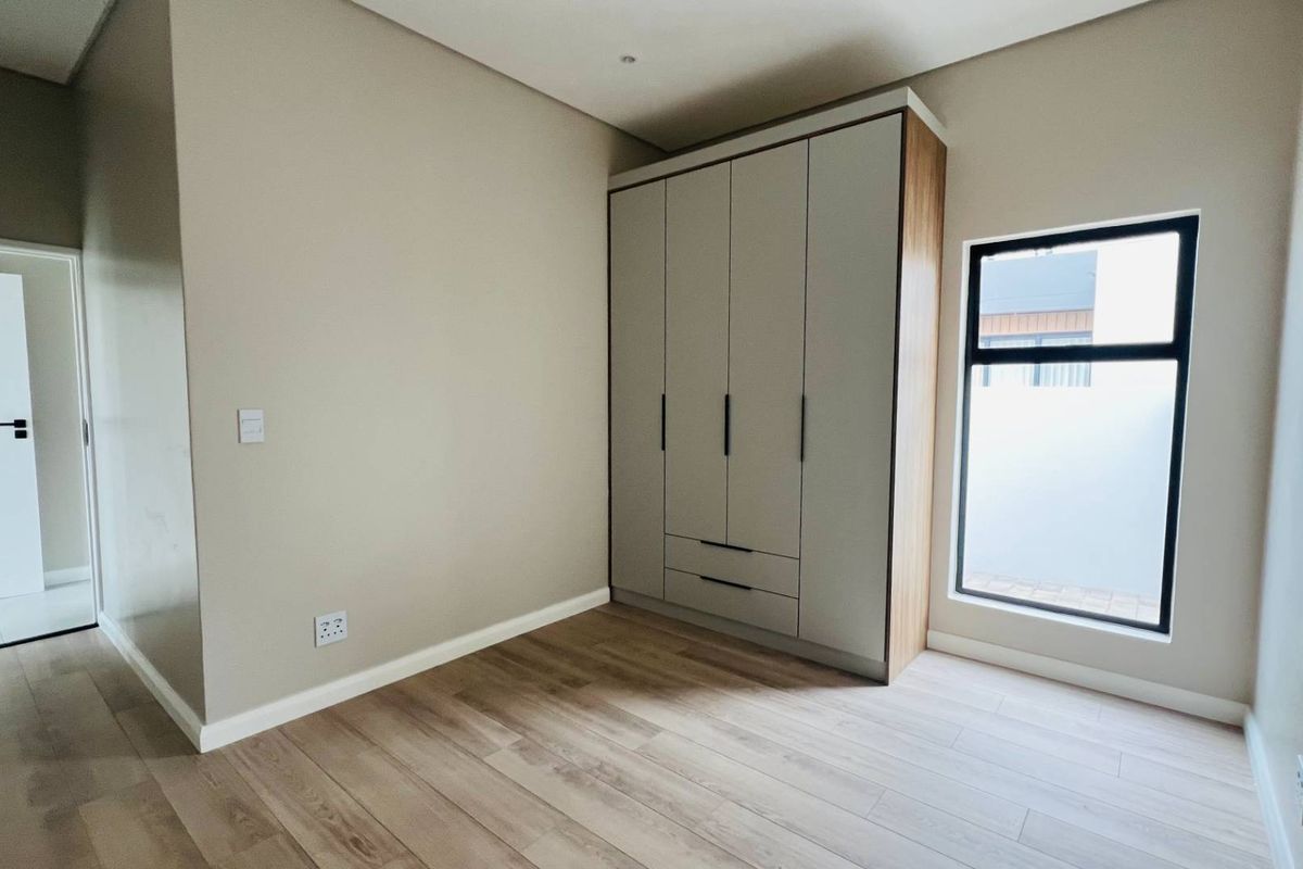 A bright, modern bedroom featuring light wood-look flooring, neutral walls, and a large, built-in wardrobe with sleek, contemporary cabinetry.