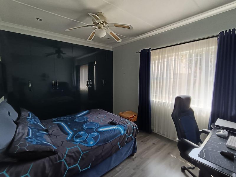 A well-maintained bedroom featuring dark built-in cupboards, a ceiling fan, and modern laminate flooring with ample natural light.