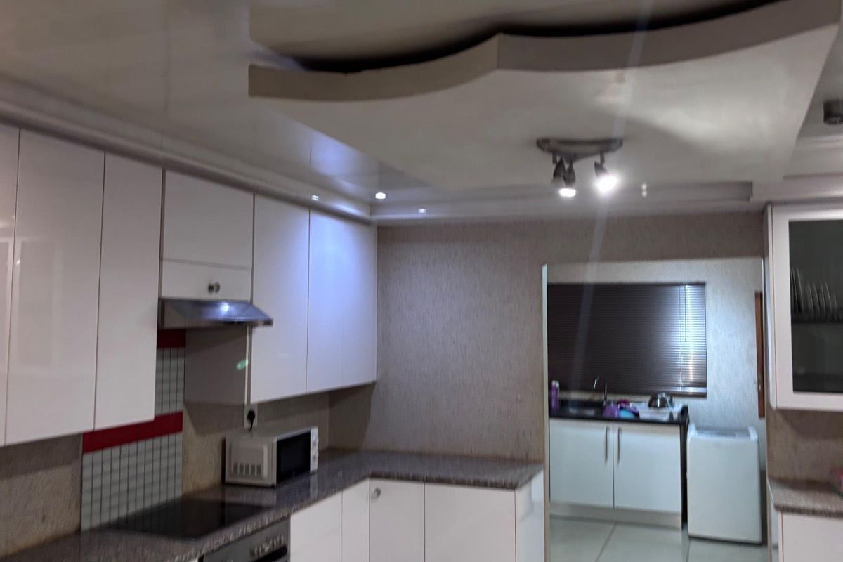 Modern kitchen featuring white high-gloss cabinetry, granite countertops, integrated appliances, and a distinctive drop ceiling with recessed lighting.