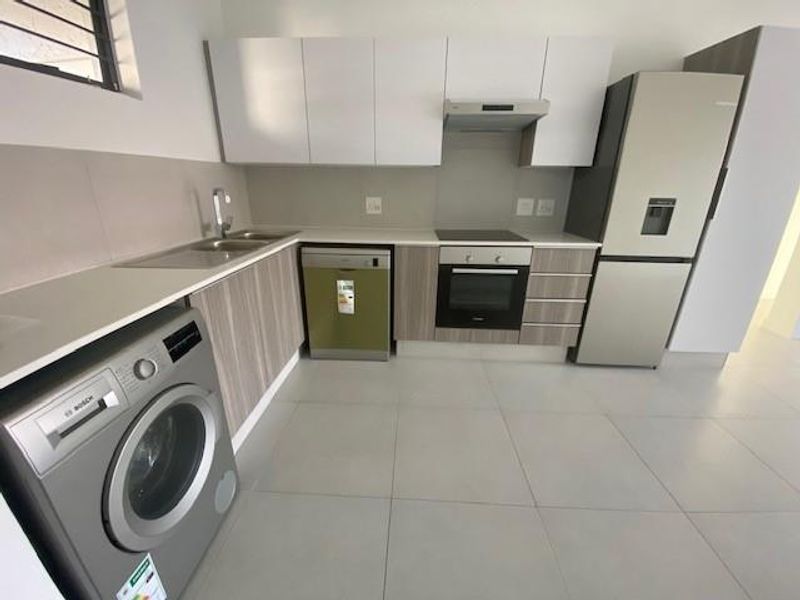 Modern kitchen featuring sleek white and wood-grain cabinetry, stone countertops, integrated electric hob, oven, extractor fan, and tiled flooring.