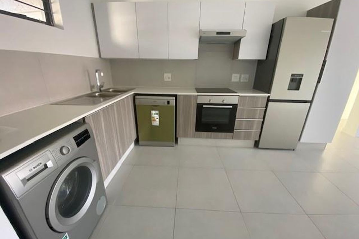 Modern kitchen featuring sleek white and wood-grain cabinetry, stone countertops, integrated electric hob, oven, extractor fan, and tiled flooring.