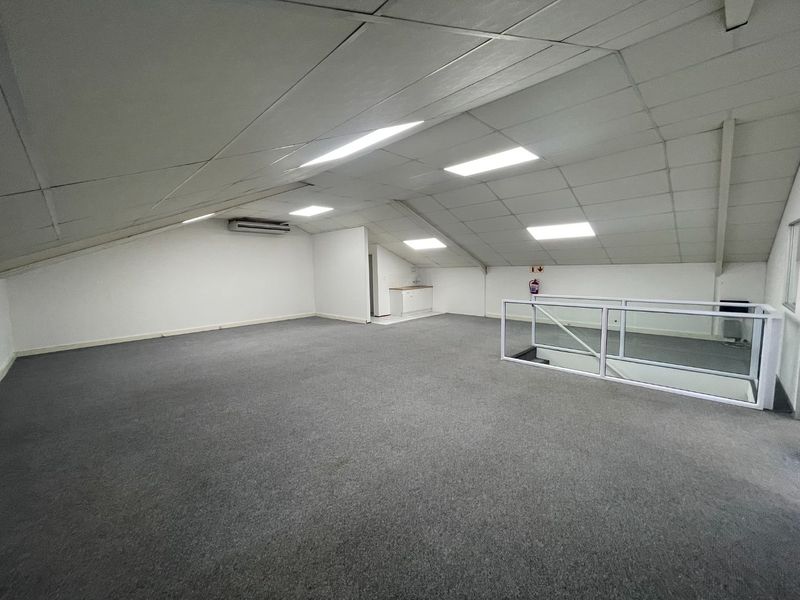 Spacious open-plan office area featuring a pitched ceiling, recessed lighting, carpeted flooring, and a glass balustrade overlooking the lower level.