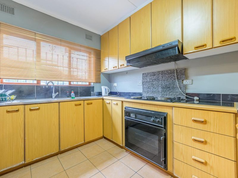 A functional kitchen featuring light wood cabinetry, built-in oven, hob, extractor fan, and tiled flooring with a neutral backsplash.