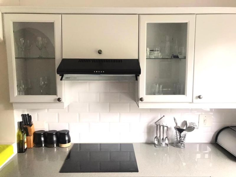 A well-maintained kitchen area featuring white cabinetry with glass inserts, a subway tile backsplash, stone countertops, and a built-in electric induction hob.