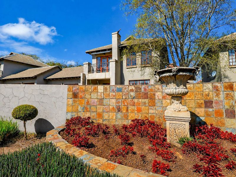Rear view of the property featuring a landscaped garden with a stone planter, a stone-clad boundary wall, and a balcony with wrought iron railings.