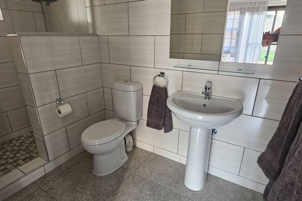 A modern, well-maintained bathroom featuring a pedestal basin, toilet, and a walk-in shower with neutral wall and floor tiling.