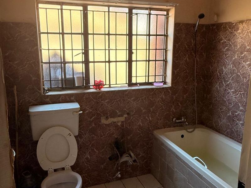 A dated bathroom featuring a bathtub, toilet, and tiled finishes, currently requiring maintenance and updates to the plumbing fixtures and wall surfaces.