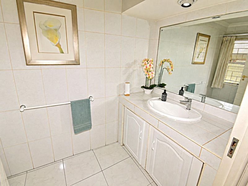 A functional bathroom featuring a tiled vanity with a built-in basin, large wall mirror, and full-height wall tiling.