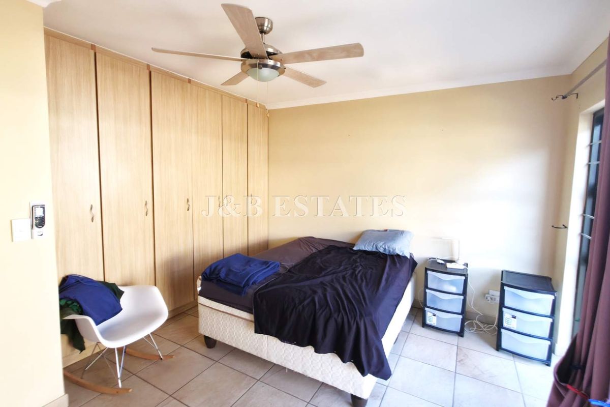 A bedroom featuring built-in wooden cupboards, a ceiling fan, and tiled flooring, offering a functional space with neutral wall finishes.