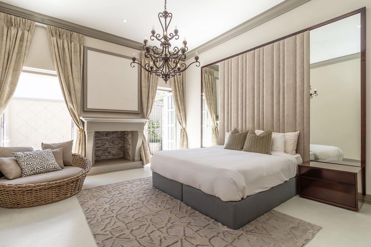 Spacious bedroom featuring a built-in fireplace, custom upholstered headboard wall, integrated mirrors, and elegant crown molding with direct access to an outdoor area.