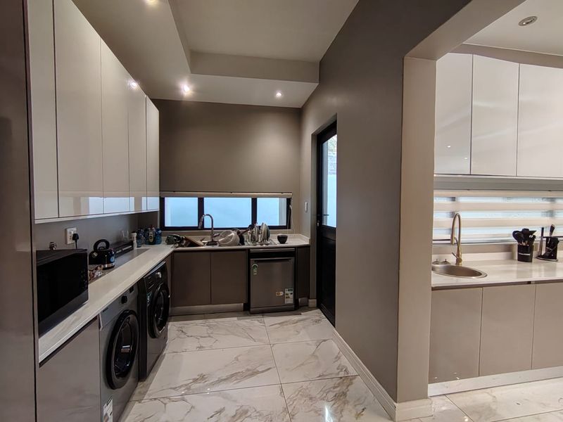 Modern scullery featuring sleek high-gloss cabinetry, stone countertops, integrated dishwasher, and premium porcelain floor tiles, providing a functional and stylish secondary kitchen area.