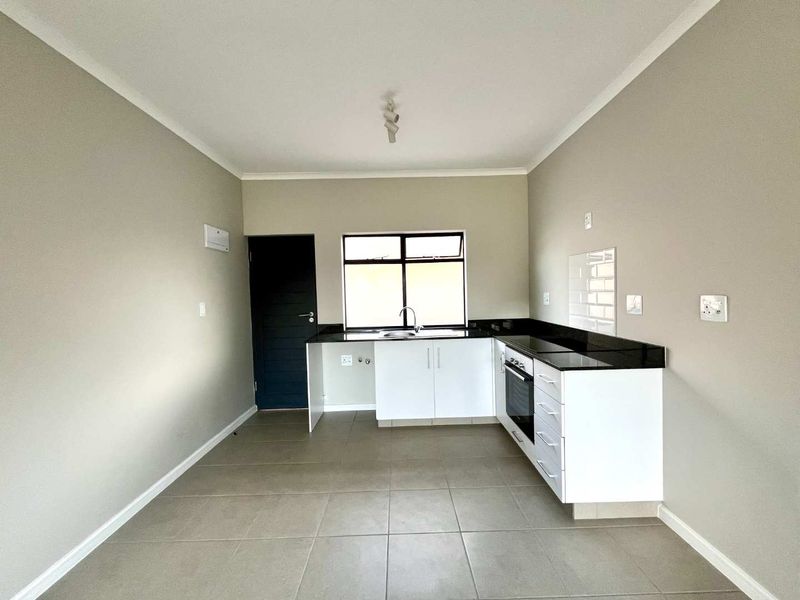 A clean, modern kitchen featuring white cabinetry, black granite countertops, built-in oven and hob, and neutral floor tiles in an open-plan layout.