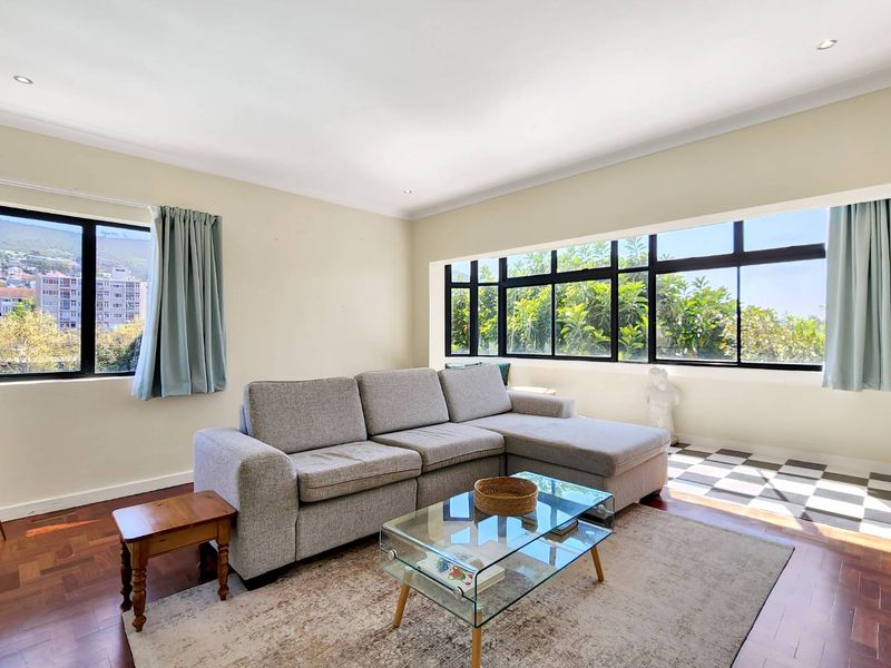 A bright living room featuring parquet flooring, large black-framed windows providing natural light, and recessed ceiling lighting.