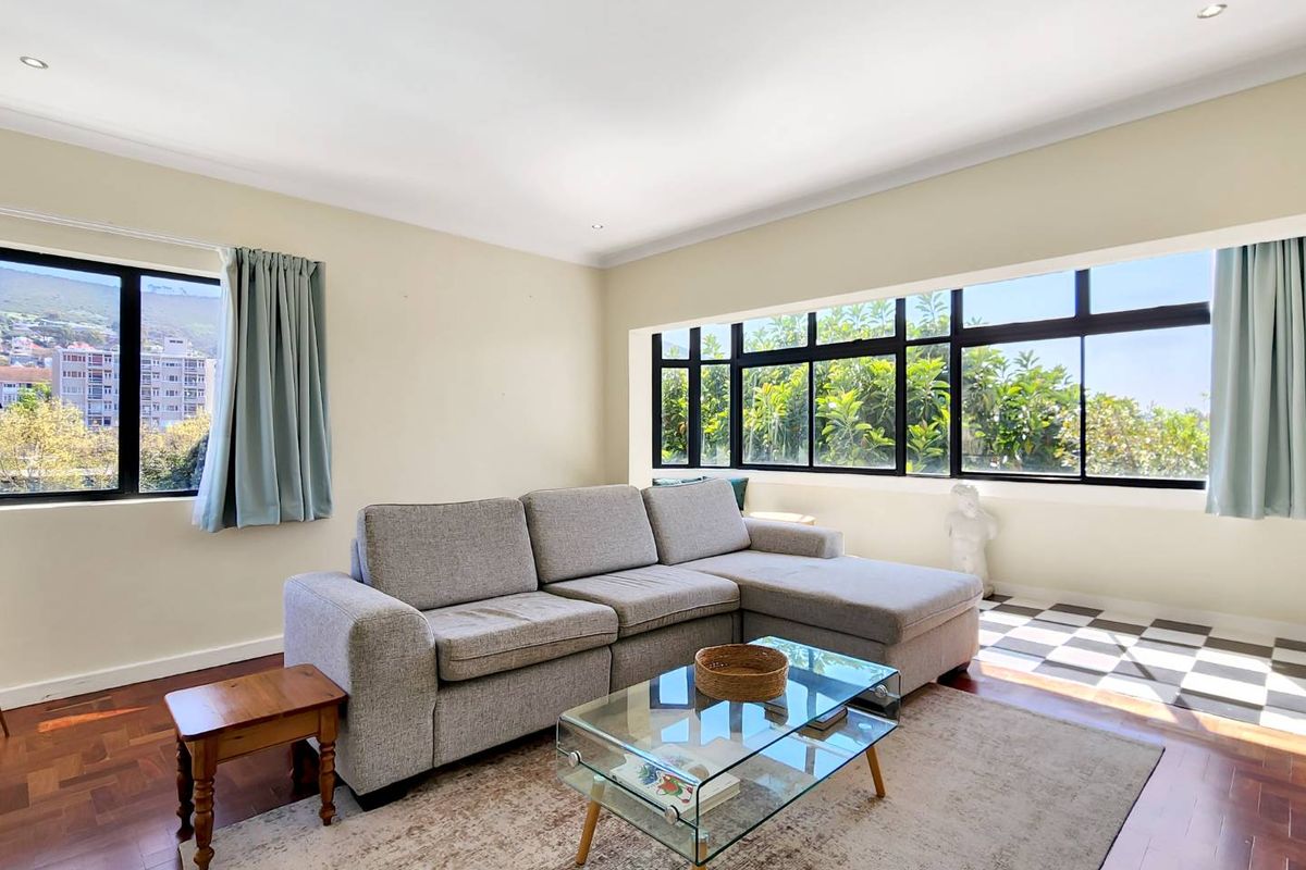 A bright living room featuring parquet flooring, large black-framed windows providing natural light, and recessed ceiling lighting.