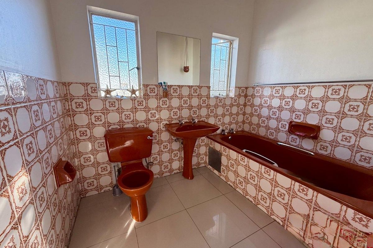 A dated bathroom featuring a terracotta-colored suite, including a bathtub, pedestal basin, and toilet, complemented by patterned wall tiles.