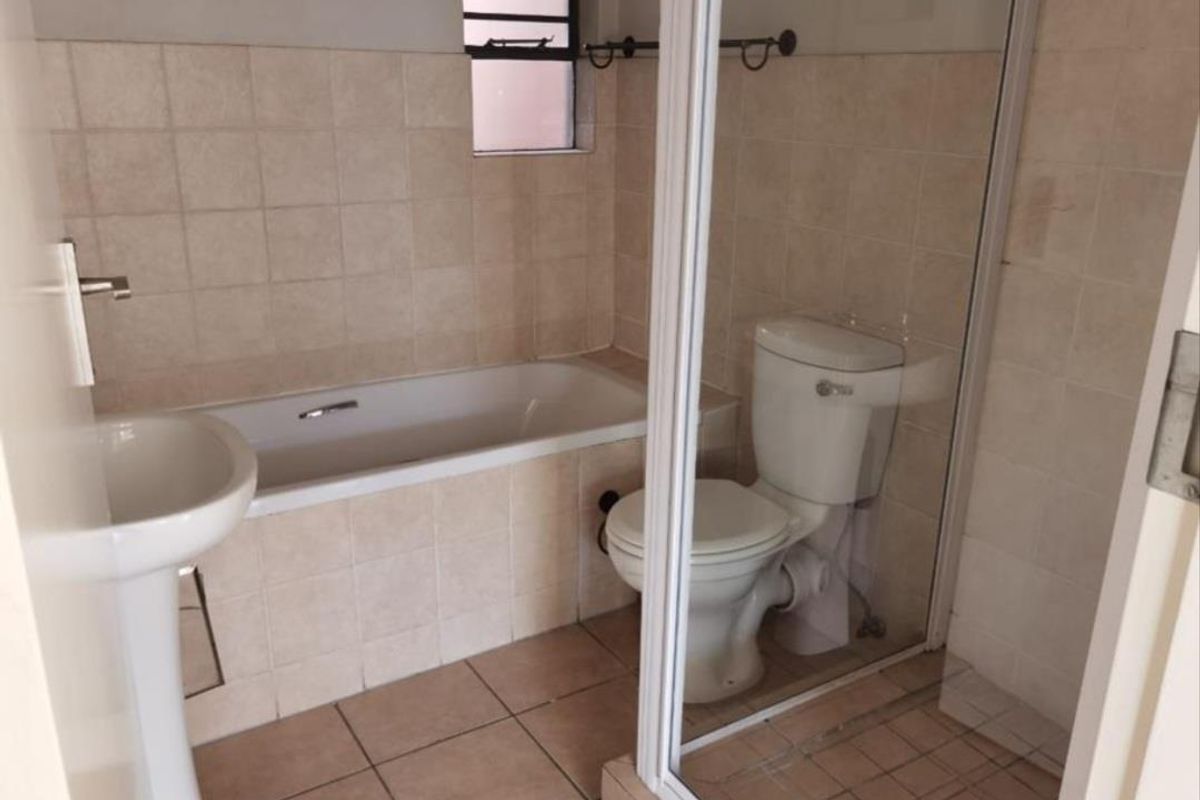 A functional bathroom featuring a pedestal basin, a built-in bathtub, and a separate glass-enclosed shower with neutral wall and floor tiling.