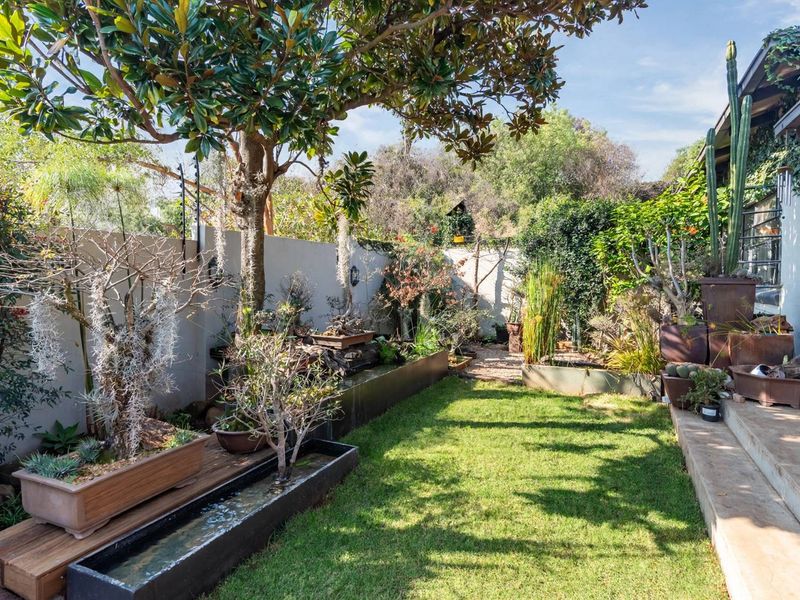 A well-maintained private garden featuring a manicured lawn, mature trees, a built-in water feature, and concrete steps leading to the house.