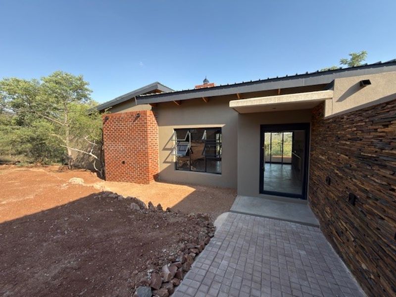 Modern front entrance featuring a combination of brick and stone cladding, a paved walkway, and contemporary aluminium window and door frames.