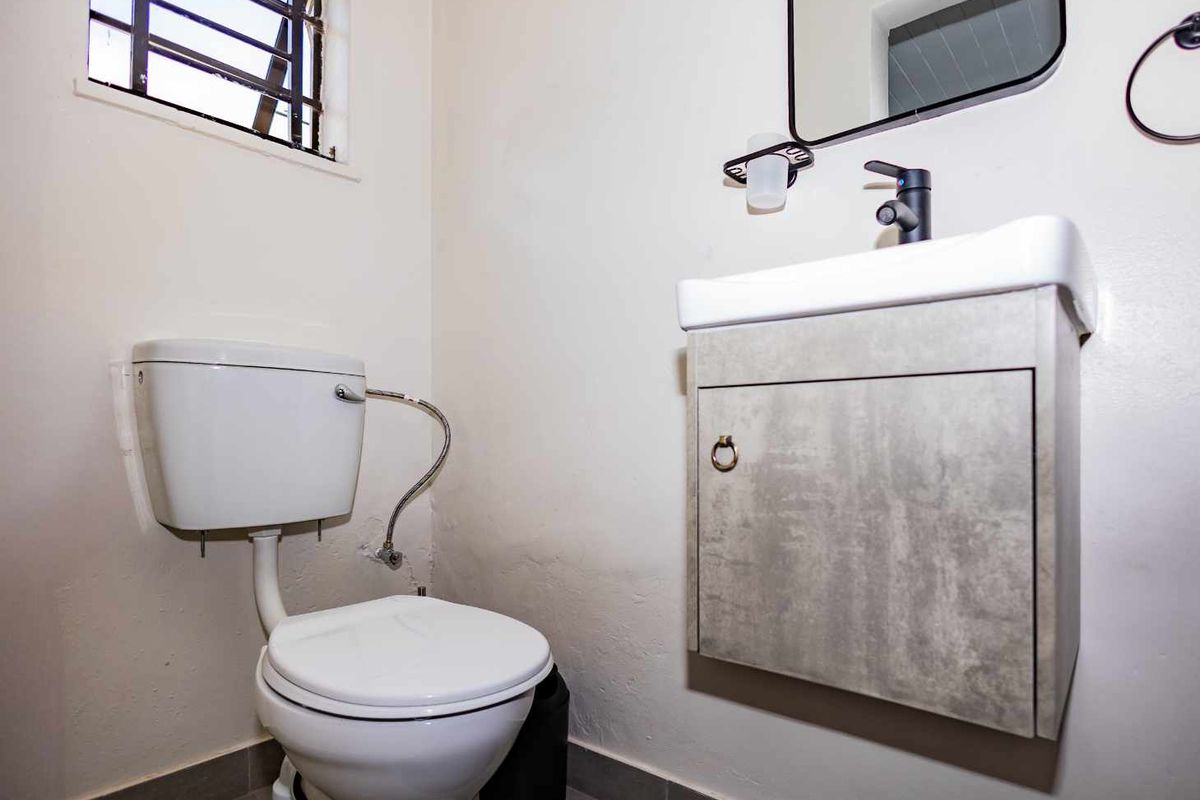 A compact bathroom featuring a wall-mounted vanity with a modern basin, a standard toilet, and a window with security bars.