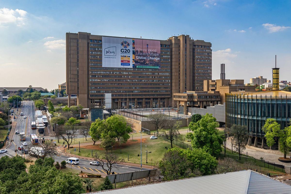 An elevated aerial view of a large urban commercial building complex surrounded by public roads, green spaces, and city infrastructure.