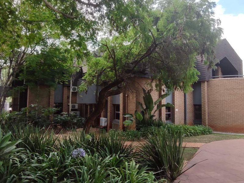 Exterior view of a face brick office building featuring a paved walkway, mature landscaping, and integrated security infrastructure.