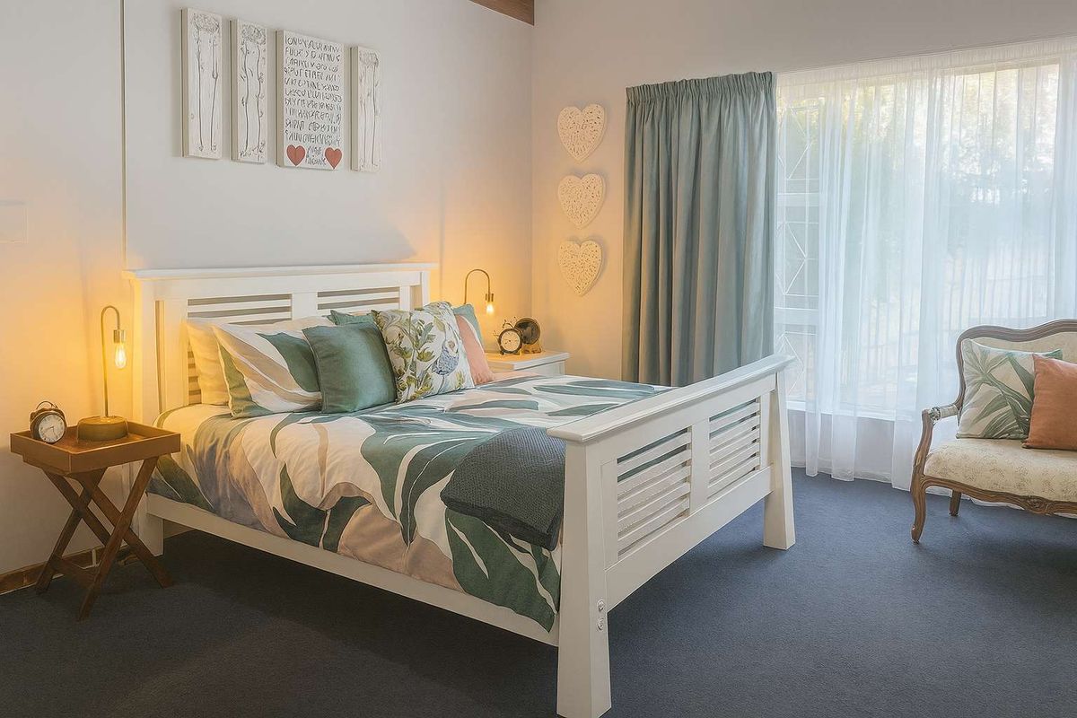 A well-maintained bedroom featuring neutral walls, dark carpeting, and a large window with curtains, providing a bright and comfortable living space.