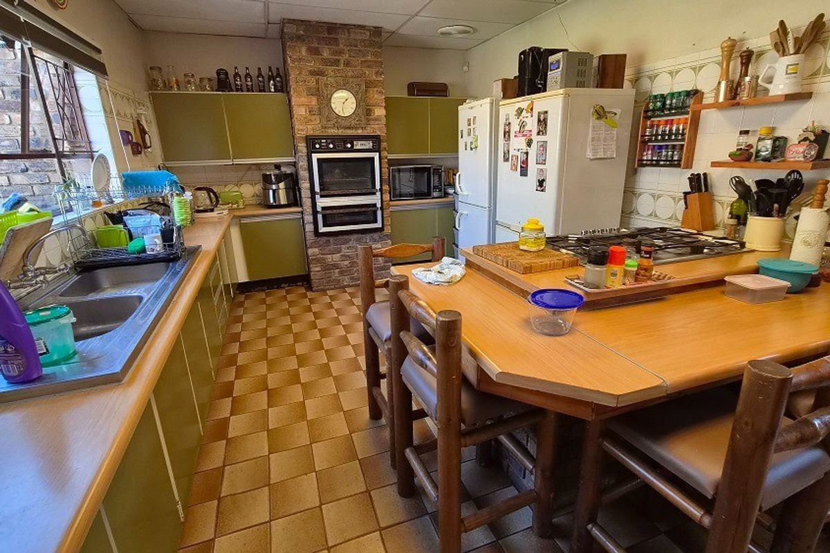 A dated kitchen featuring a brick chimney breast, built-in oven, gas hob, double sink, and ample cabinetry with a central breakfast bar area.