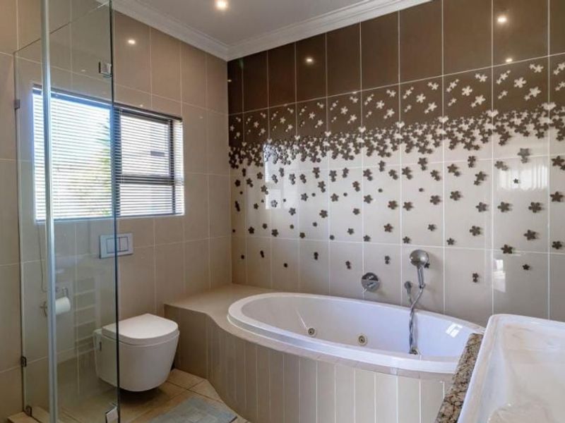 Modern bathroom featuring a built-in jetted bathtub, glass-enclosed shower, wall-mounted toilet, and decorative tiled feature wall.