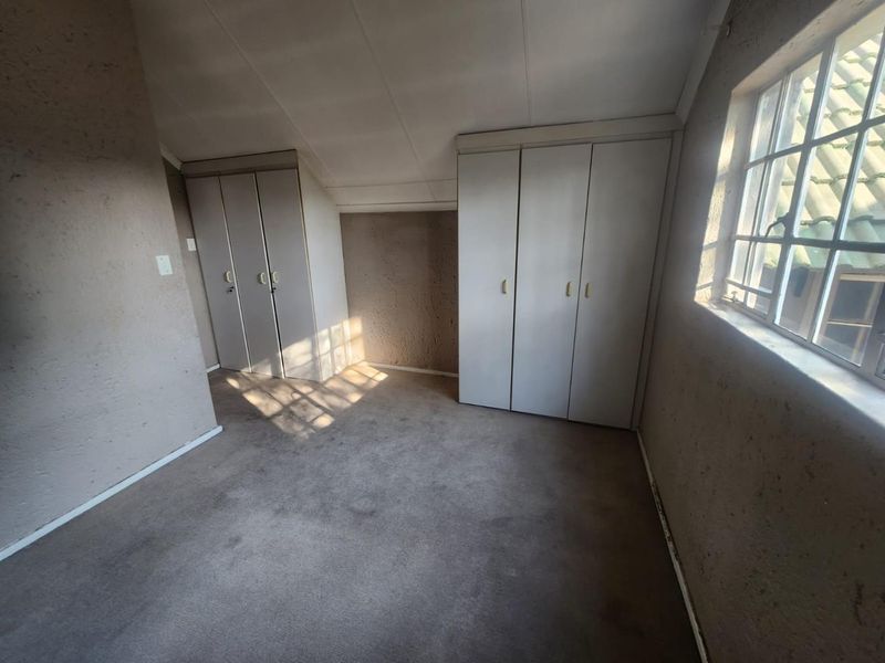 An empty bedroom featuring built-in cupboards, carpeted flooring, and a sloped ceiling, offering a blank canvas for renovation.