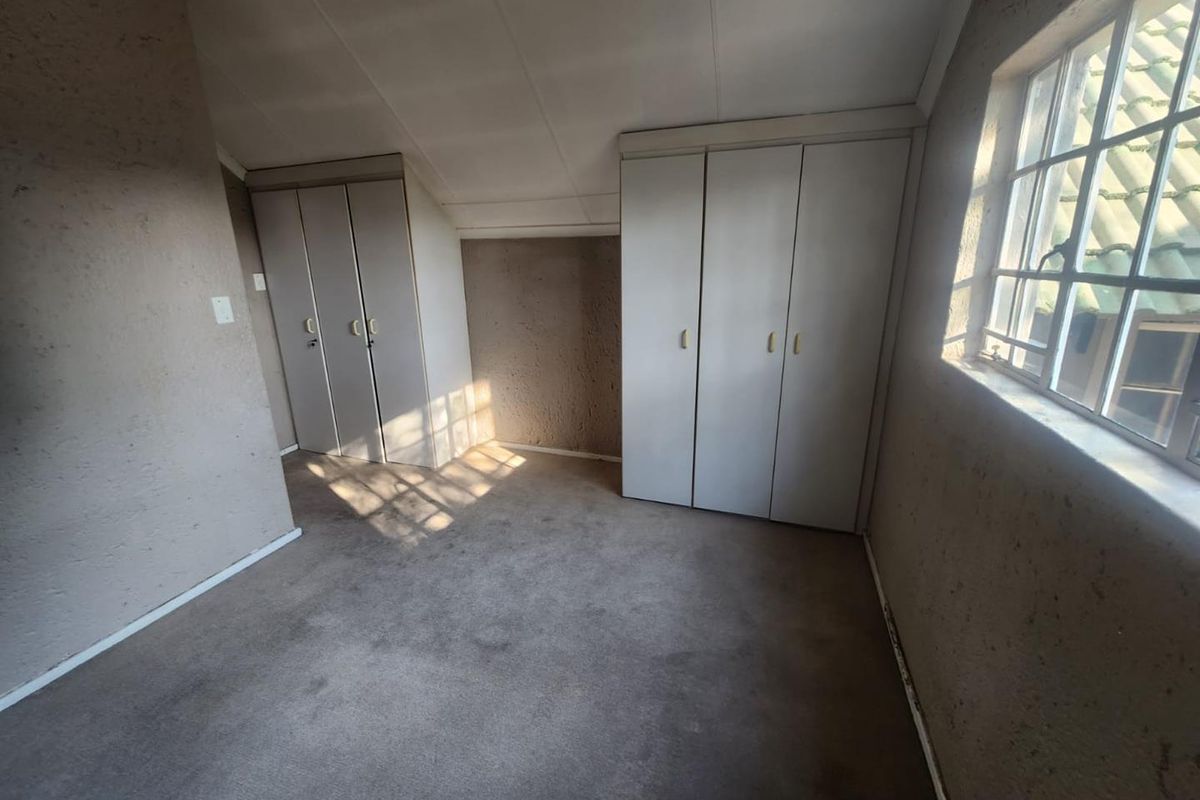 An empty bedroom featuring built-in cupboards, carpeted flooring, and a sloped ceiling, offering a blank canvas for renovation.
