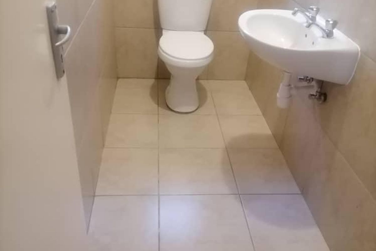 A compact guest bathroom featuring neutral wall and floor tiling, a wall-mounted basin, and a standard toilet.