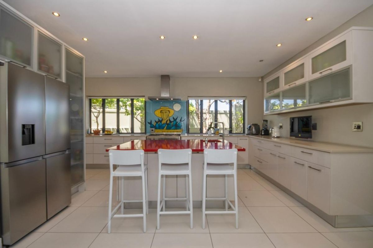 Modern kitchen featuring a central island with a red countertop, sleek cabinetry, integrated stainless steel appliances, and recessed ceiling lighting.