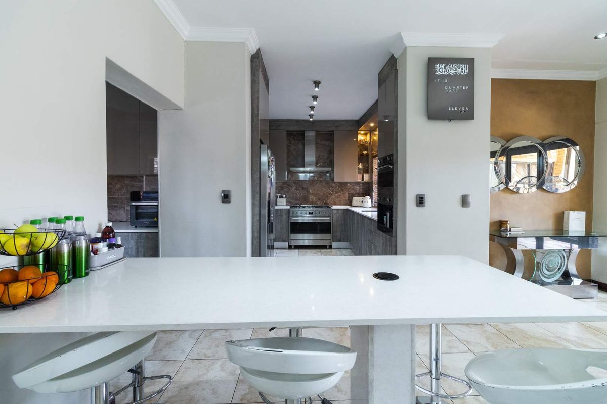 Modern kitchen featuring stone countertops, a breakfast bar, built-in oven, gas stove, and an adjacent scullery area with tiled flooring throughout.