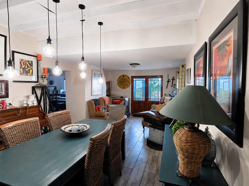 Open plan dining and living area featuring exposed ceiling beams, modern pendant lighting, and tiled flooring with access to the exterior through glass panel doors.