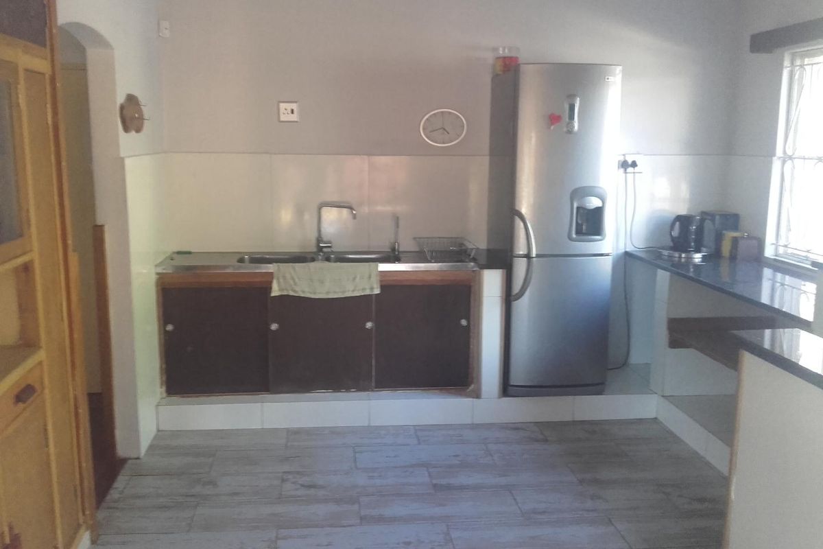 A functional kitchen area featuring tiled flooring, a double sink, and granite-style countertops with built-in cabinetry.