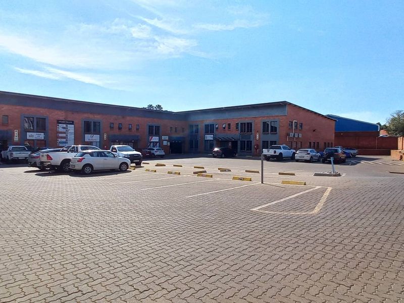 Exterior view of an industrial business park featuring a paved parking area and multi-unit brick facade buildings.